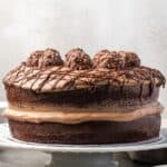 Side view of chocolate hazelnut cake filled and decorated with mousse, topped with chocolate hazelnut candy on a cake stand.