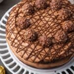 Overhead view of chocolate hazelnut cake drizzled with chocolate and topped with chocolate hazelnut candy on a cake stand.