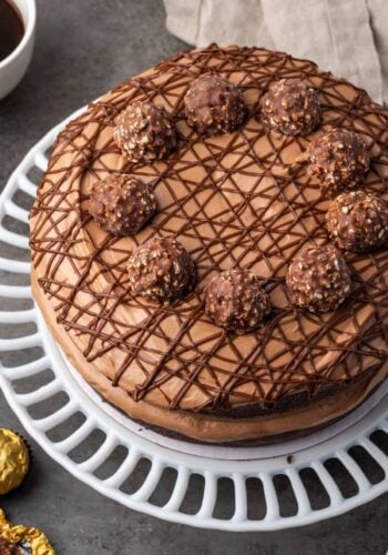 Overhead view of chocolate hazelnut cake drizzled with chocolate and topped with chocolate hazelnut candy on a cake stand.