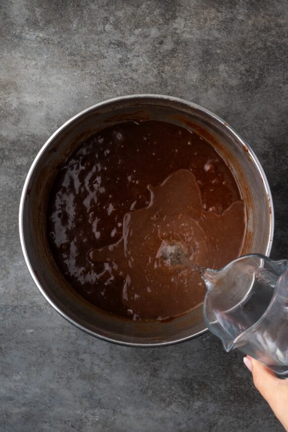 Hot water being added to chocolate cake batter in a metal bowl.