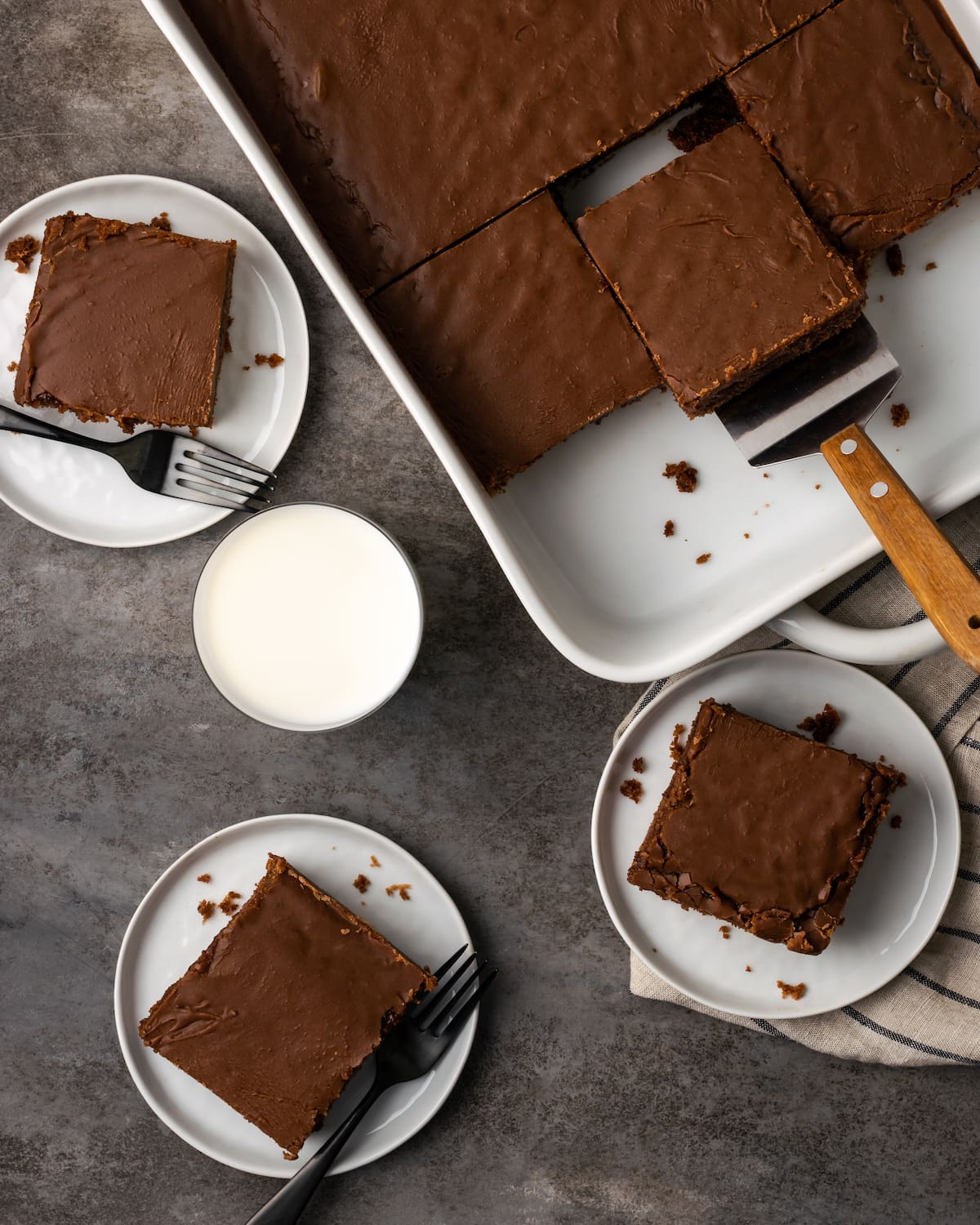 Overhead view of slices of chocolate sheet cake served on plates next to more cake in a baking dish.