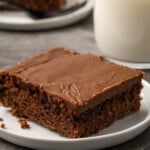 A slice of Sunday chocolate sheet cake on plate next to a glass of milk.