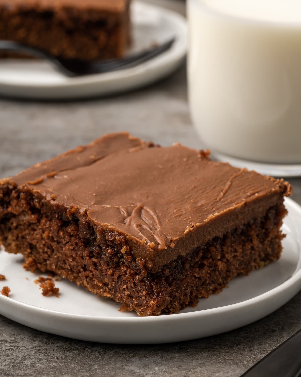 A slice of Sunday chocolate sheet cake on plate next to a glass of milk.