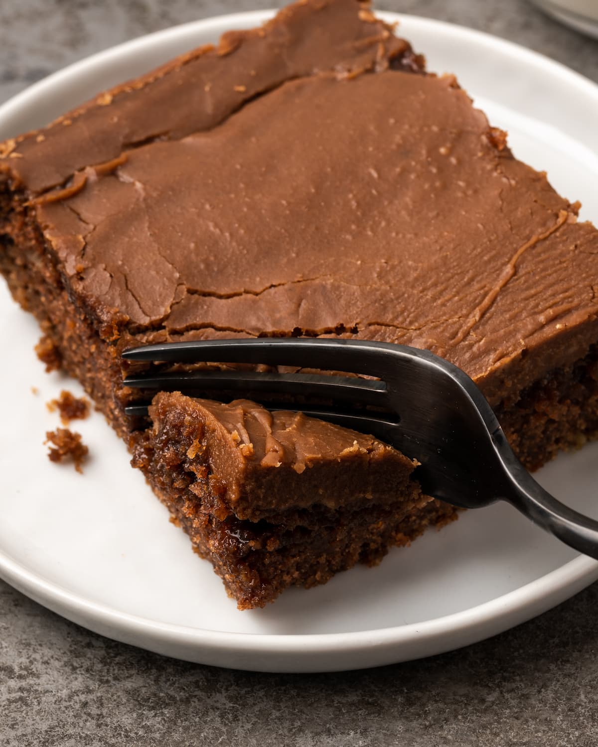A fork cuts into a slice of chocolate sheet cake on a white plate.