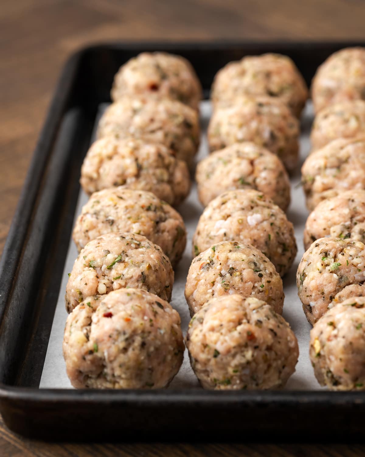 Rows of rolled turkey meatballs on a parchment-lined baking sheet.