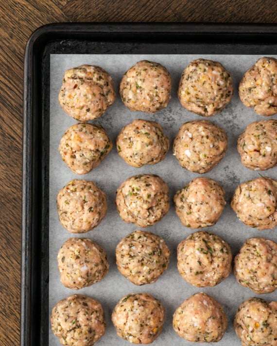 Top view of rows of rolled turkey meatballs on a parchment-lined baking sheet.