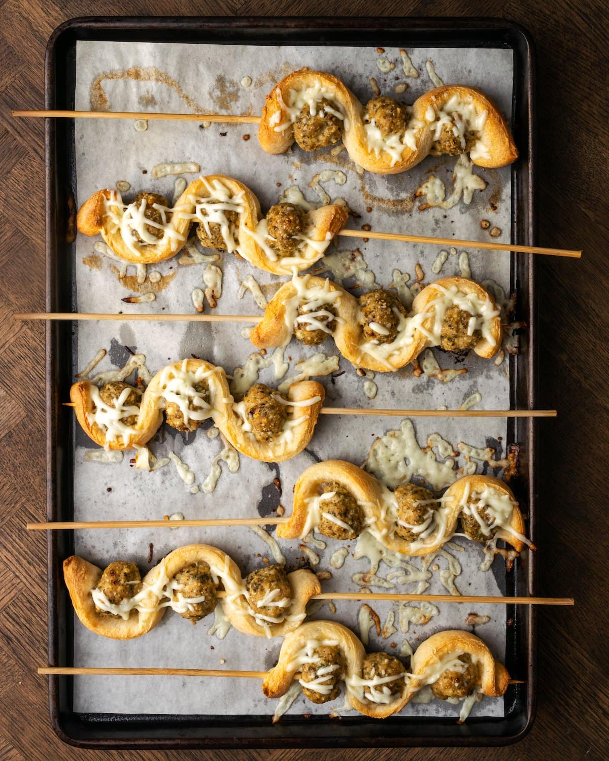 Top view of baked meatball subs on a stick lined up on a parchment-lined baking sheet.