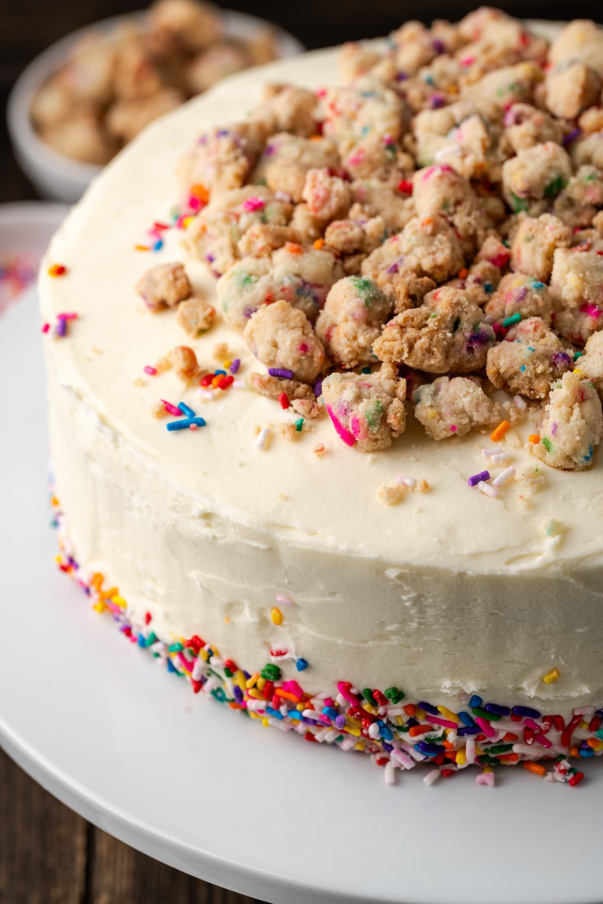 Frosted confetti cake decorated with sprinkles and a crumbled funfetti streusel topping.