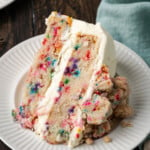 A slice of frosted confetti cake on a white plate.