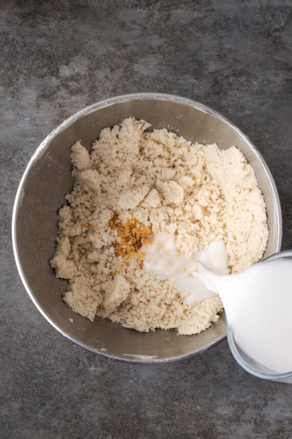 Milk and vanilla added to cake batter ingredients in a metal mixing bowl.