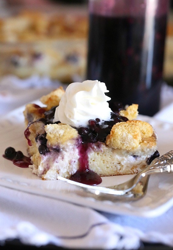 A slice of blueberry French toast casserole topped with blueberry sauce and whipped cream on a plate.