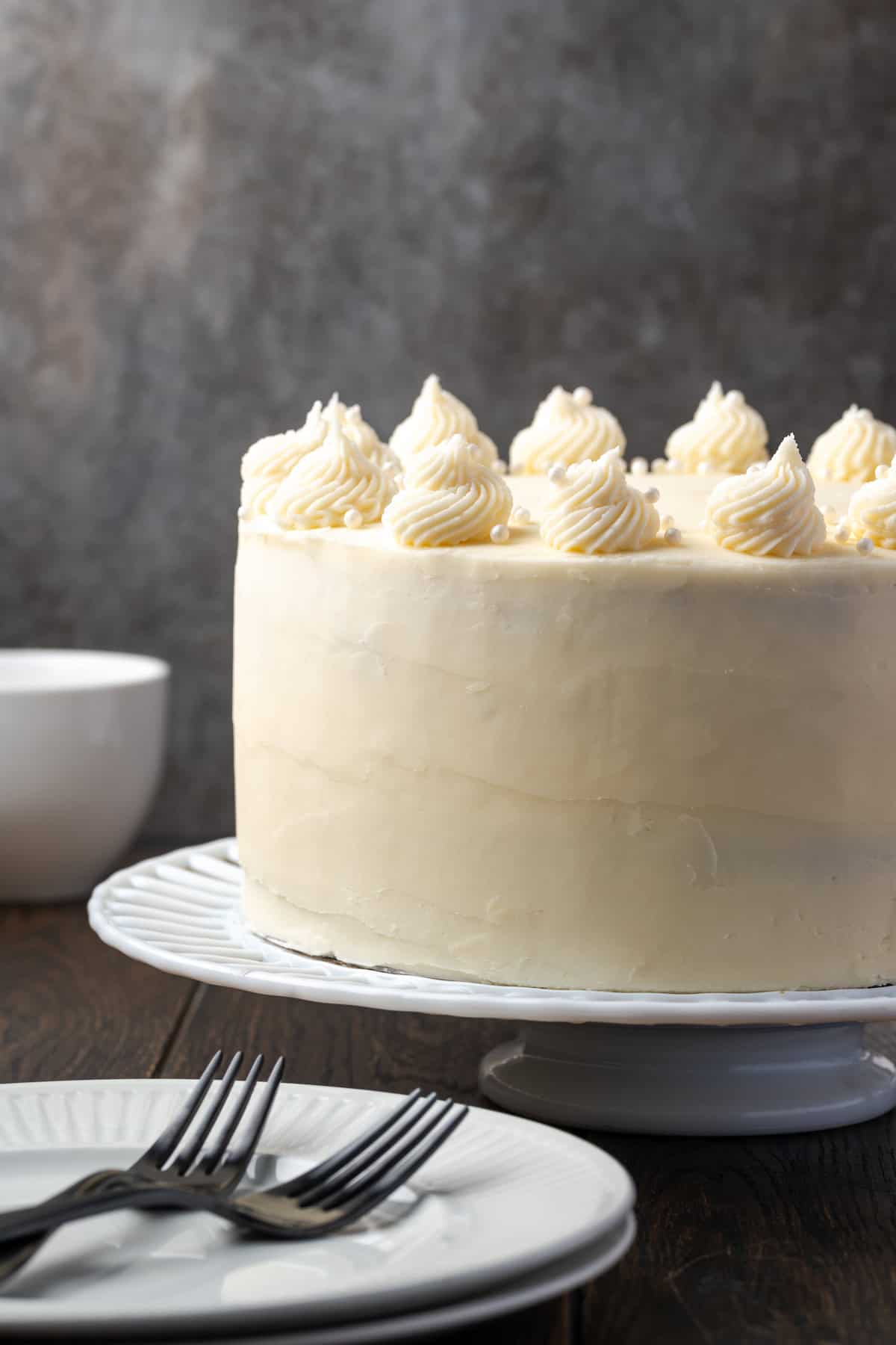 Side view of a frosted vanilla layer cake on a cake stand.