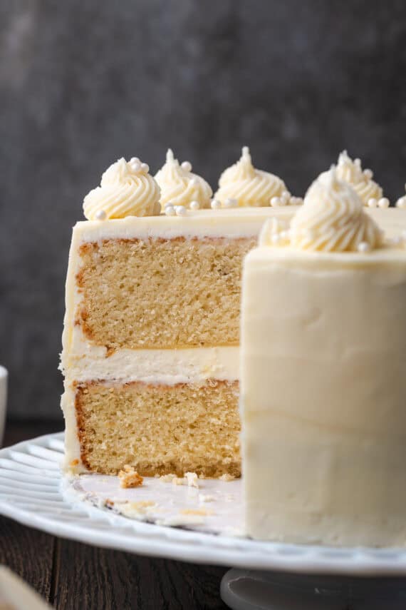 Side view of a frosted vanilla layer cake with a large slice missing.