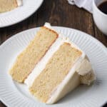 A slice of vanilla cake on a white plate, with a second slice in the background.