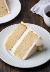 A slice of vanilla cake on a white plate, with a second slice in the background.