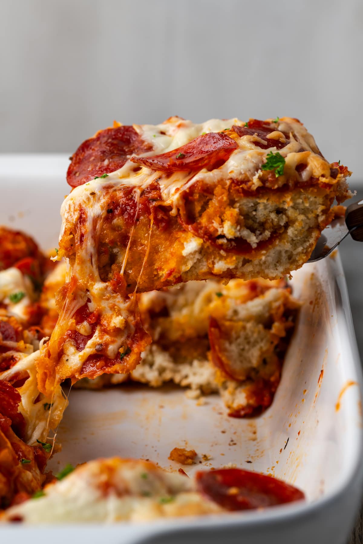 A serving of pizza casserole is lifted from a baking dish.