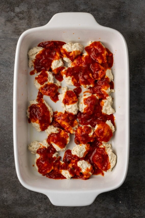 Pizza sauce layered over pieces of Bisquick dough in a baking dish.