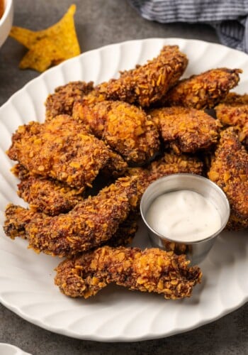 Crispy ranch chicken tenders arranged around a small metal ramekin of ranch dressing on a white platter.
