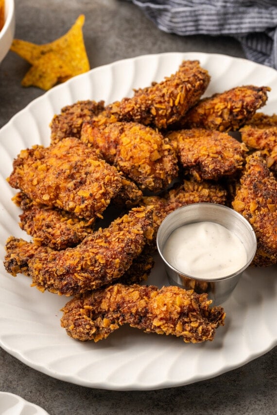 Crispy ranch chicken tenders arranged around a small metal ramekin of ranch dressing on a white platter.