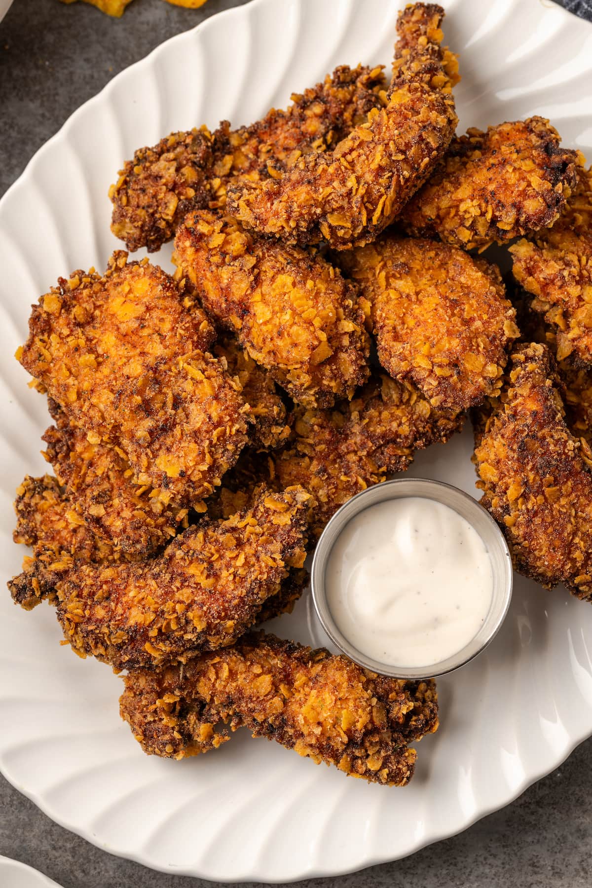Overhead view of crispy ranch chicken tenders arranged around a small metal ramekin of ranch dressing on a white platter.