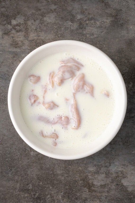 Chicken tenders soaking in a bowl of buttermilk.