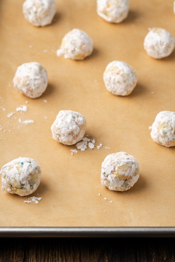 Funfetti cookie dough balls coated in powdered sugar arranged on a parchment-lined baking sheet.
