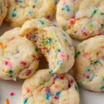 Close up of assorted funfetti cookies on a parchment-lined baking sheet, with a bite missing from one cookie.