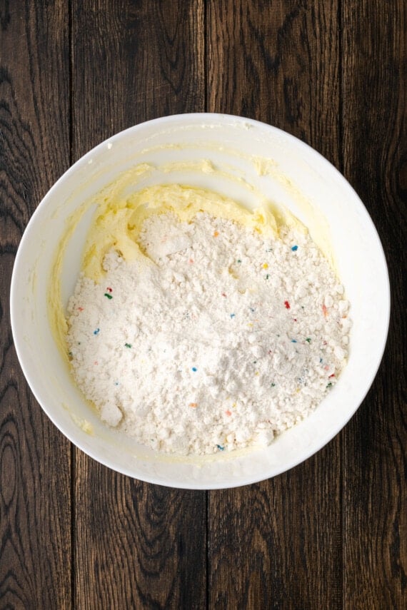 Funfetti cake mix added to a bowl with creamed butter and cream cheese.