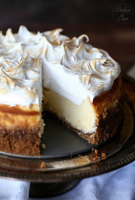 A Lemon Meringue Cheesecake on a cake stand with a slice missing.