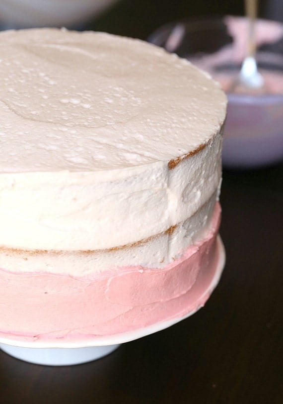 This pink lemonade cake is ultra-soft and bursting with bright, juicy flavor from lemonade and fresh lemon zest in the cake and frosting. Frosting a cake in a pink ombre frosting.