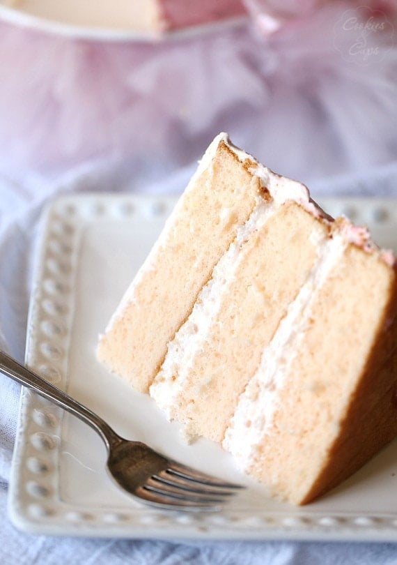 This pink lemonade cake is ultra-soft and bursting with bright, juicy flavor from lemonade and fresh lemon zest in the cake and frosting. A slice of pink lemonade cake showing three frosted layers on a plate.