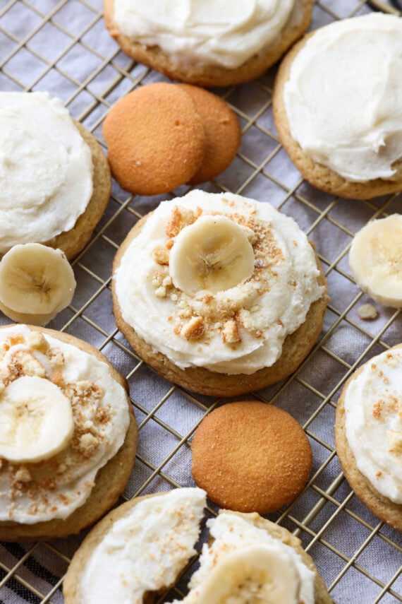 A slice of banana on top of a frosted banana cookie surrounded by cookies and banana slices.