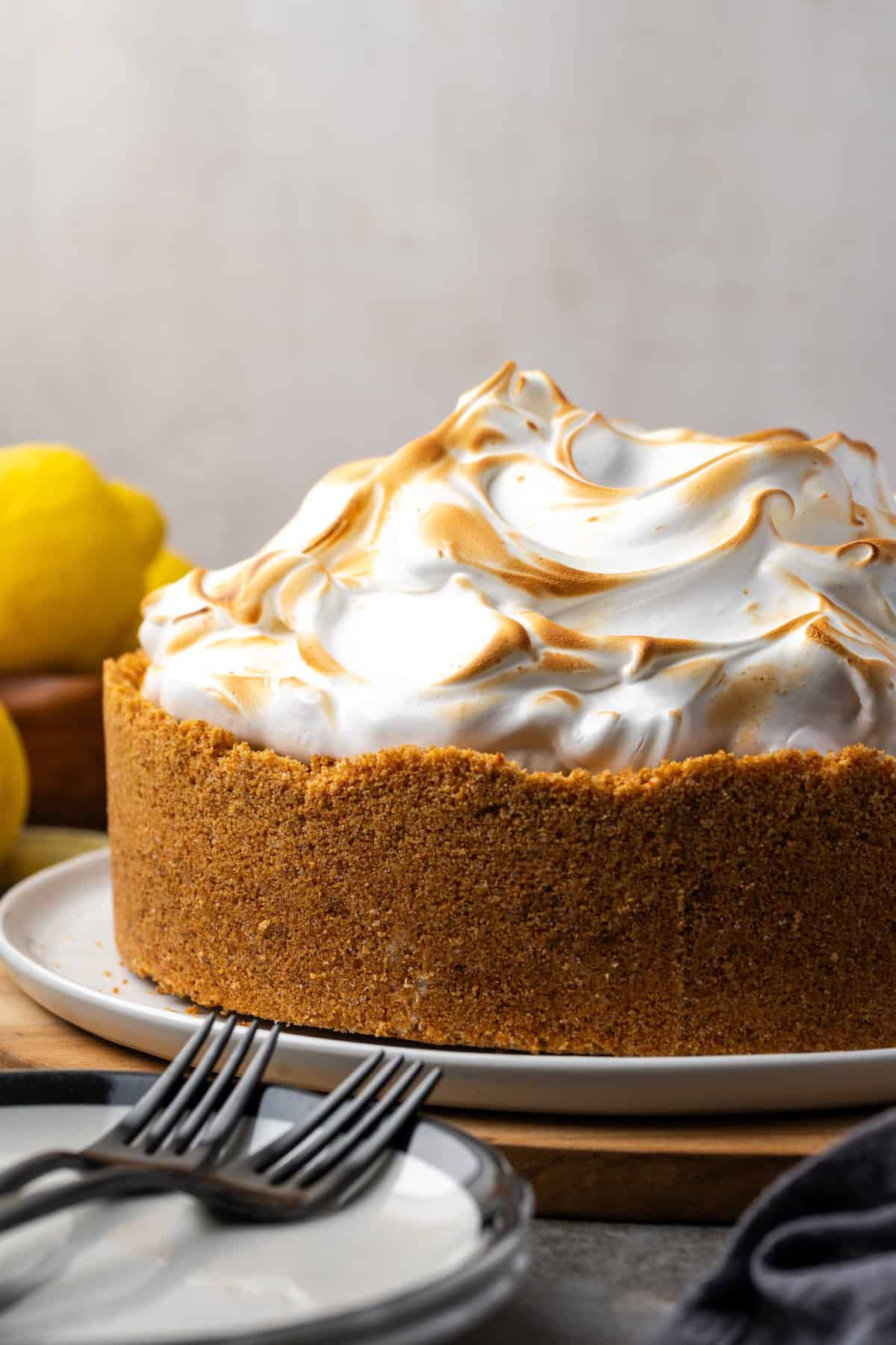 This zesty lemon meringue cheesecake has a smooth and creamy lemon filling, buttery graham cracker crust, and pillows of homemade meringue! Side view of lemon meringue cheesecake with a toasted top on a plate.