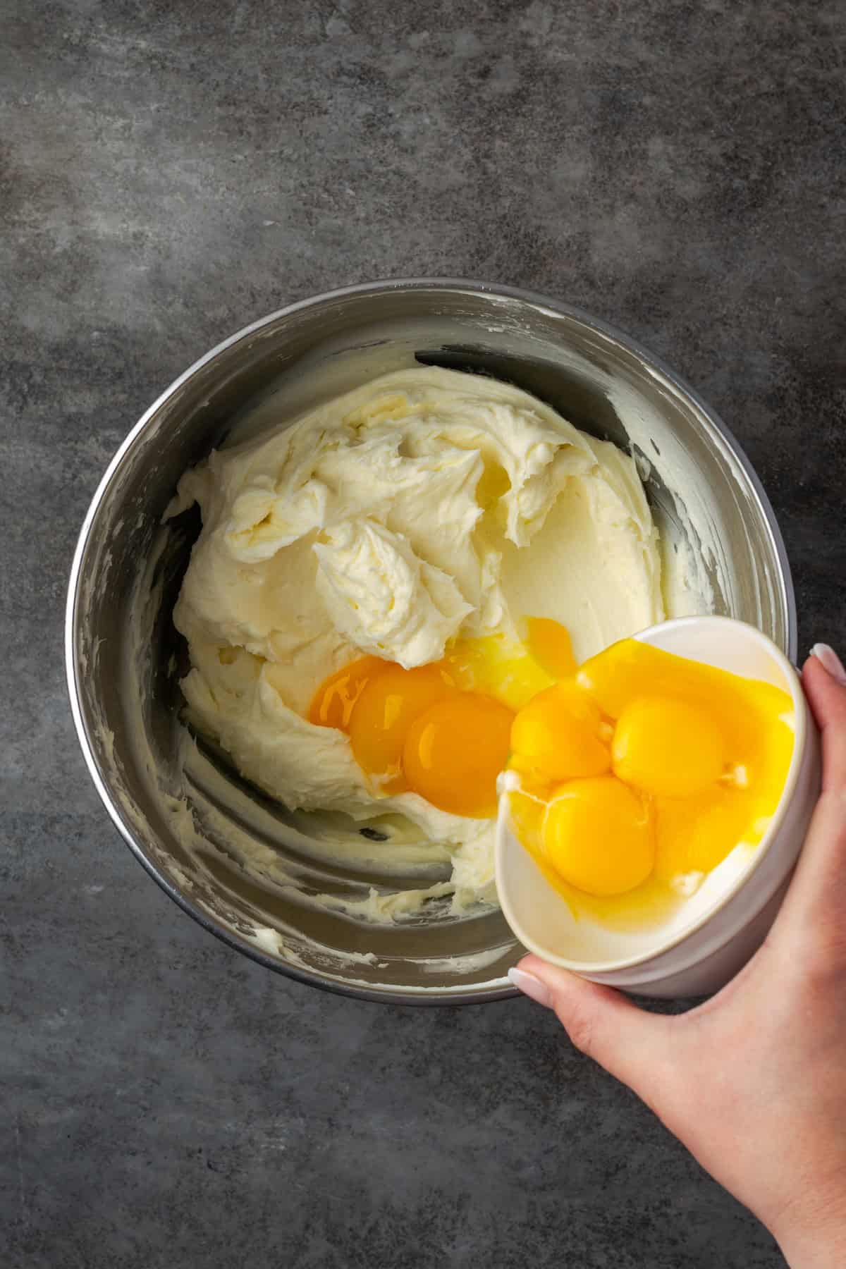 This zesty lemon meringue cheesecake has a smooth and creamy lemon filling, buttery graham cracker crust, and pillows of homemade meringue! A hand pouring egg yolks from a small bowl into cheesecake filling in a bowl.