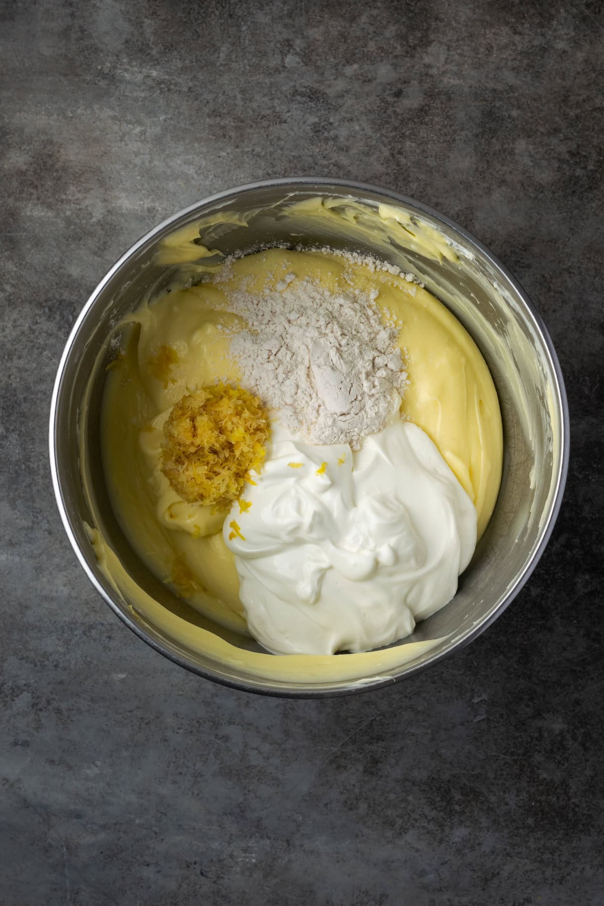 This zesty lemon meringue cheesecake has a smooth and creamy lemon filling, buttery graham cracker crust, and pillows of homemade meringue! Sour cream, lemon zest, and flour added to cheesecake filling in a bowl.