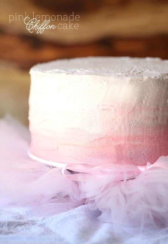 This pink lemonade cake is ultra-soft and bursting with bright, juicy flavor from lemonade and fresh lemon zest in the cake and frosting. Side view of a pink lemonade layer cake frosted with pink ombré frosting on a cake stand.