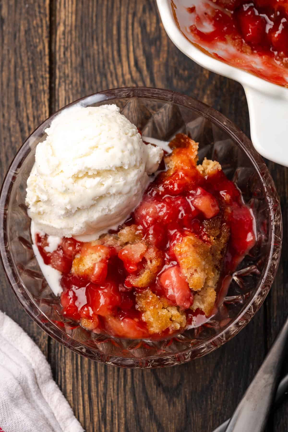 Overhead view of a serving of strawberry cobbler in a bowl topped with vanilla ice cream.