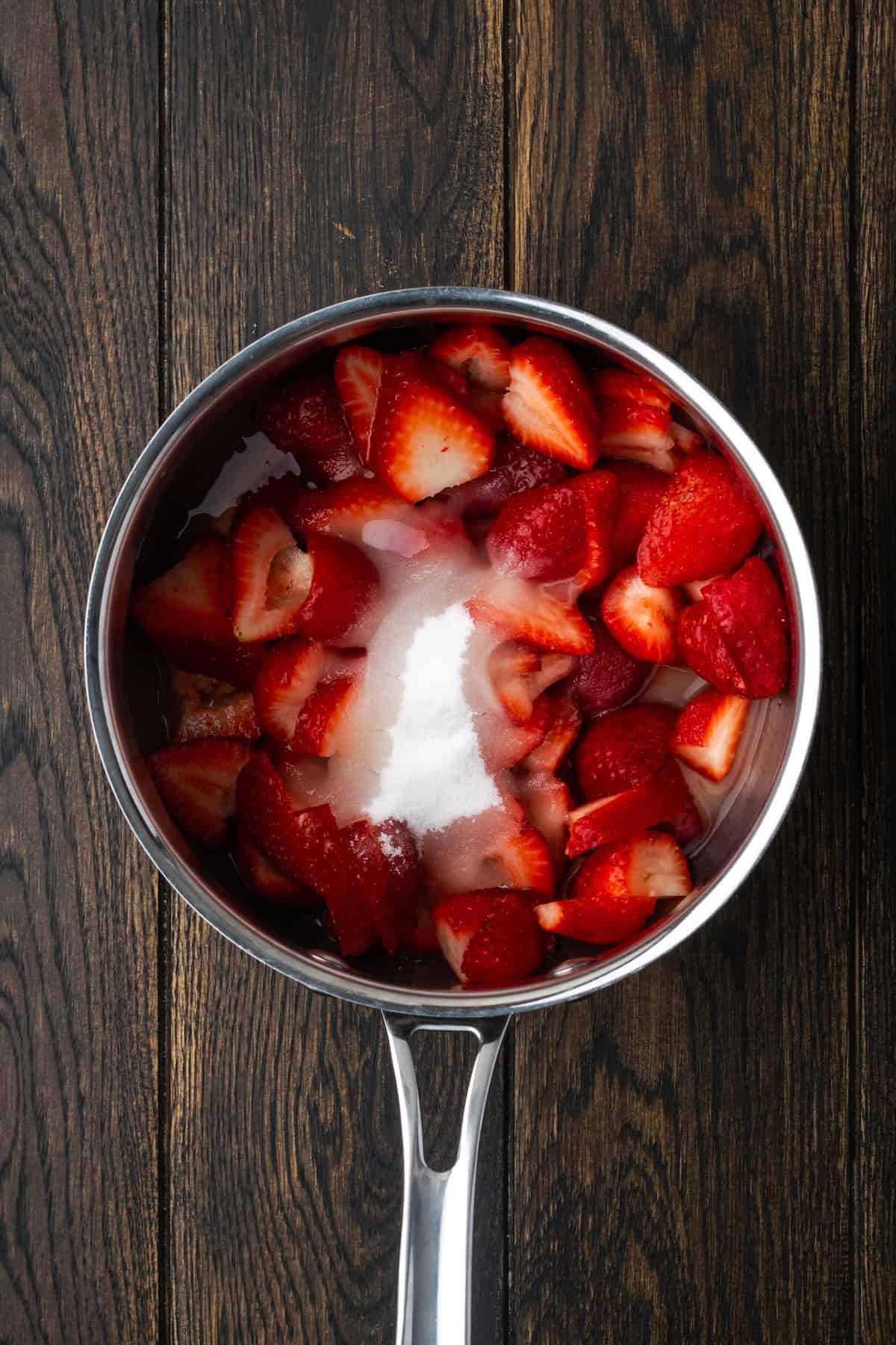 Sugar added to chopped strawberries in a saucepan.