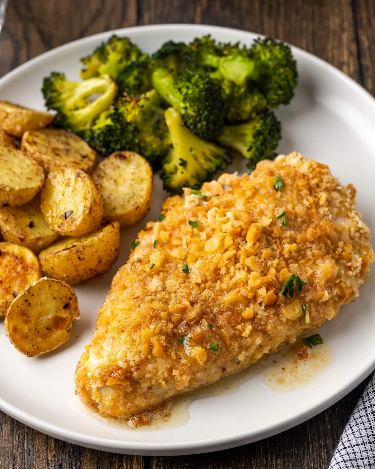 Baked chicken breast on a plate with potatoes and broccoli.