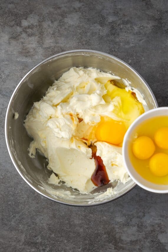 Eggs being added to the cheesecake filling in a bowl.