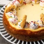 Sugar cookie cheesecake topped with swirls of sprinkle whipped cream and broken cookies.