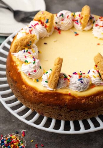 Sugar cookie cheesecake topped with swirls of sprinkle whipped cream and broken cookies.