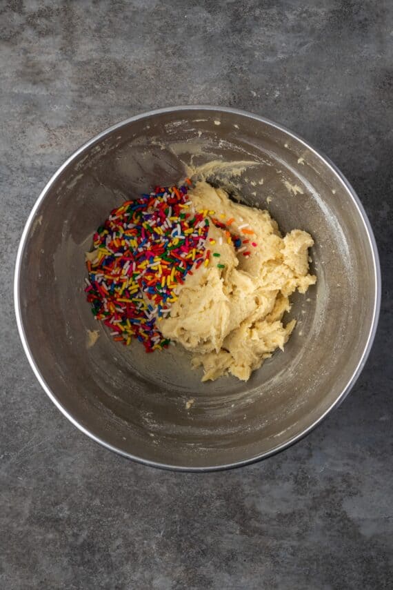 Rainbow sprinkles added to sugar cookie dough in a mixing bowl.