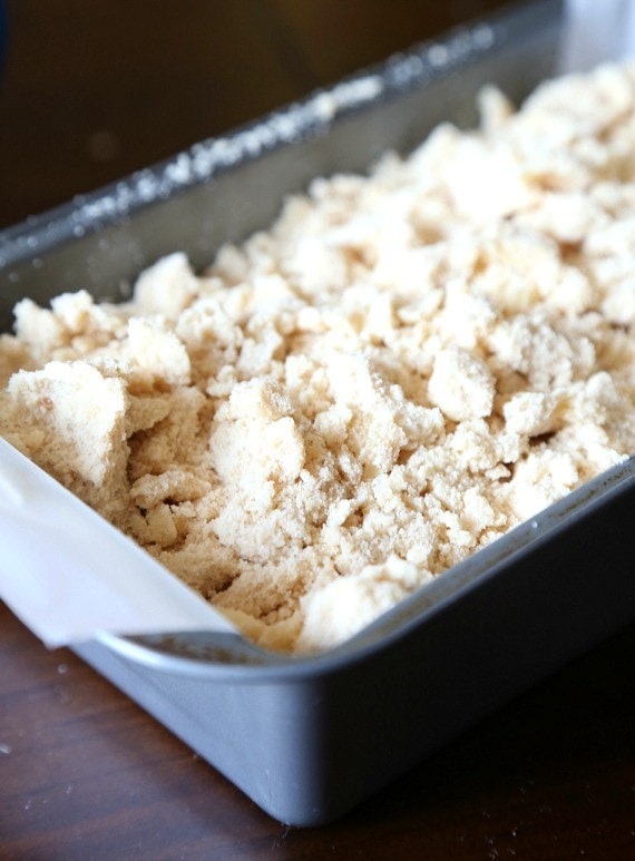 Blueberry bread batter topped with a crumble in a parchment-lined loaf pan.