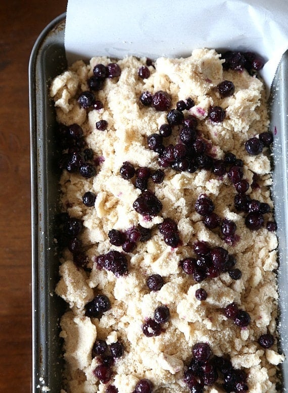 Overhead view of blueberry bread batter topped with blueberries in a parchment-lined loaf pan.