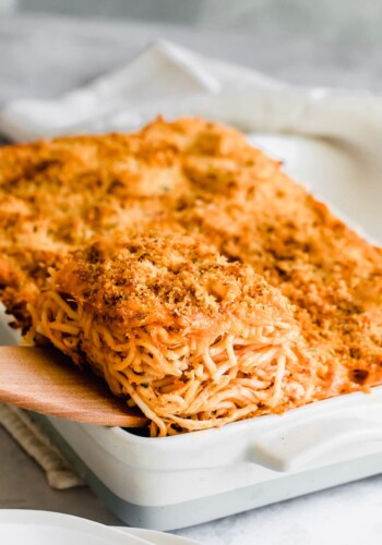 A wooden spatula lifts a serving of chicken spaghetti casserole from a baking dish.