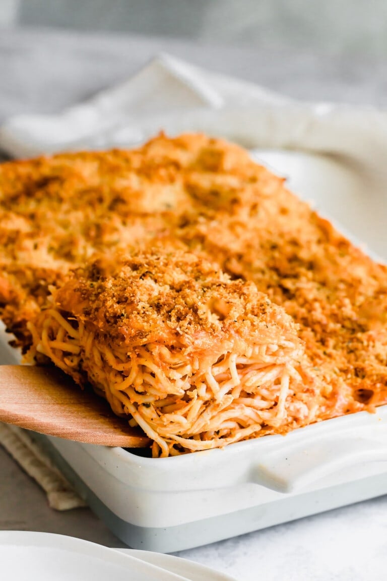 A wooden spatula lifts the chicken spaghetti casserole from the baking dish.