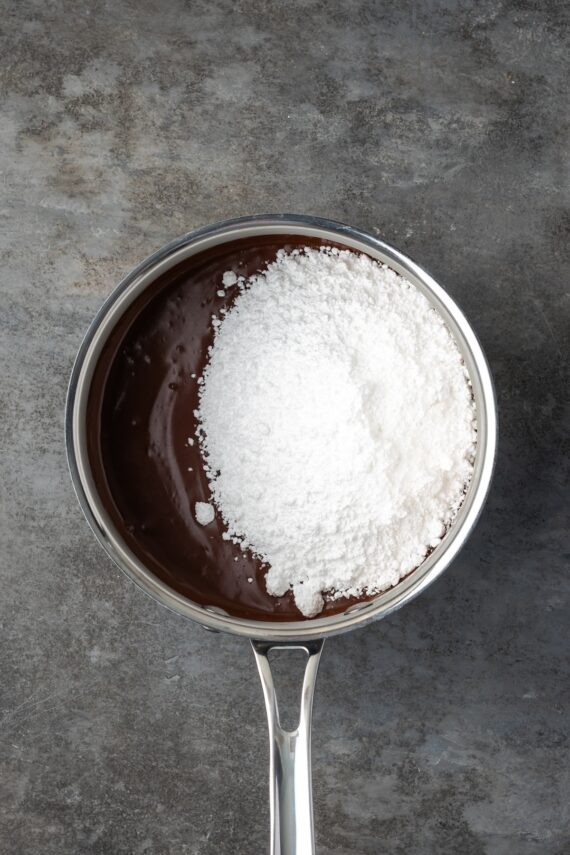 Powdered sugar added to chocolate frosting in a saucepan.