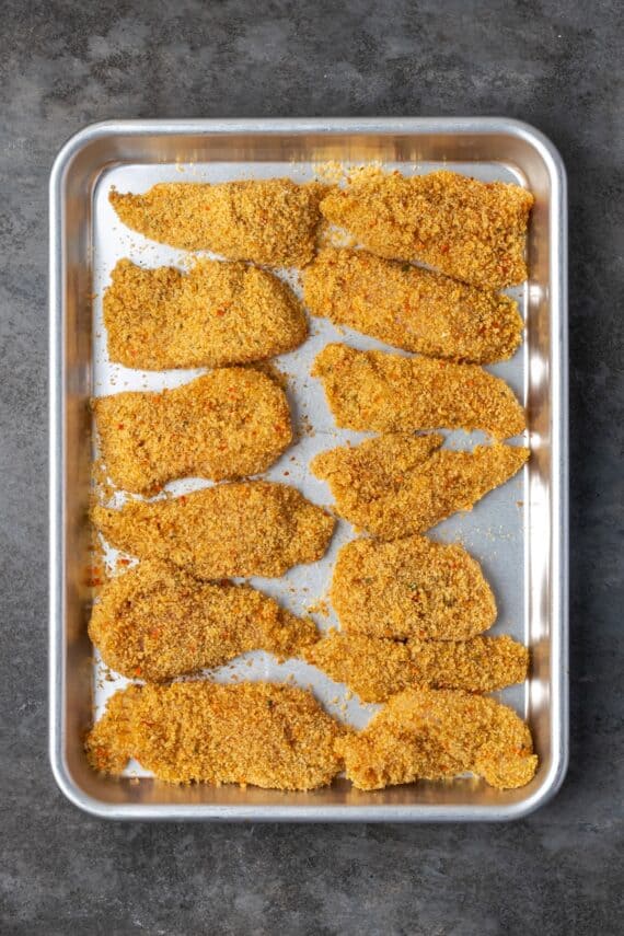 Overhead view of chicken cutlets breaded with chicken stuffing on a baking sheet.