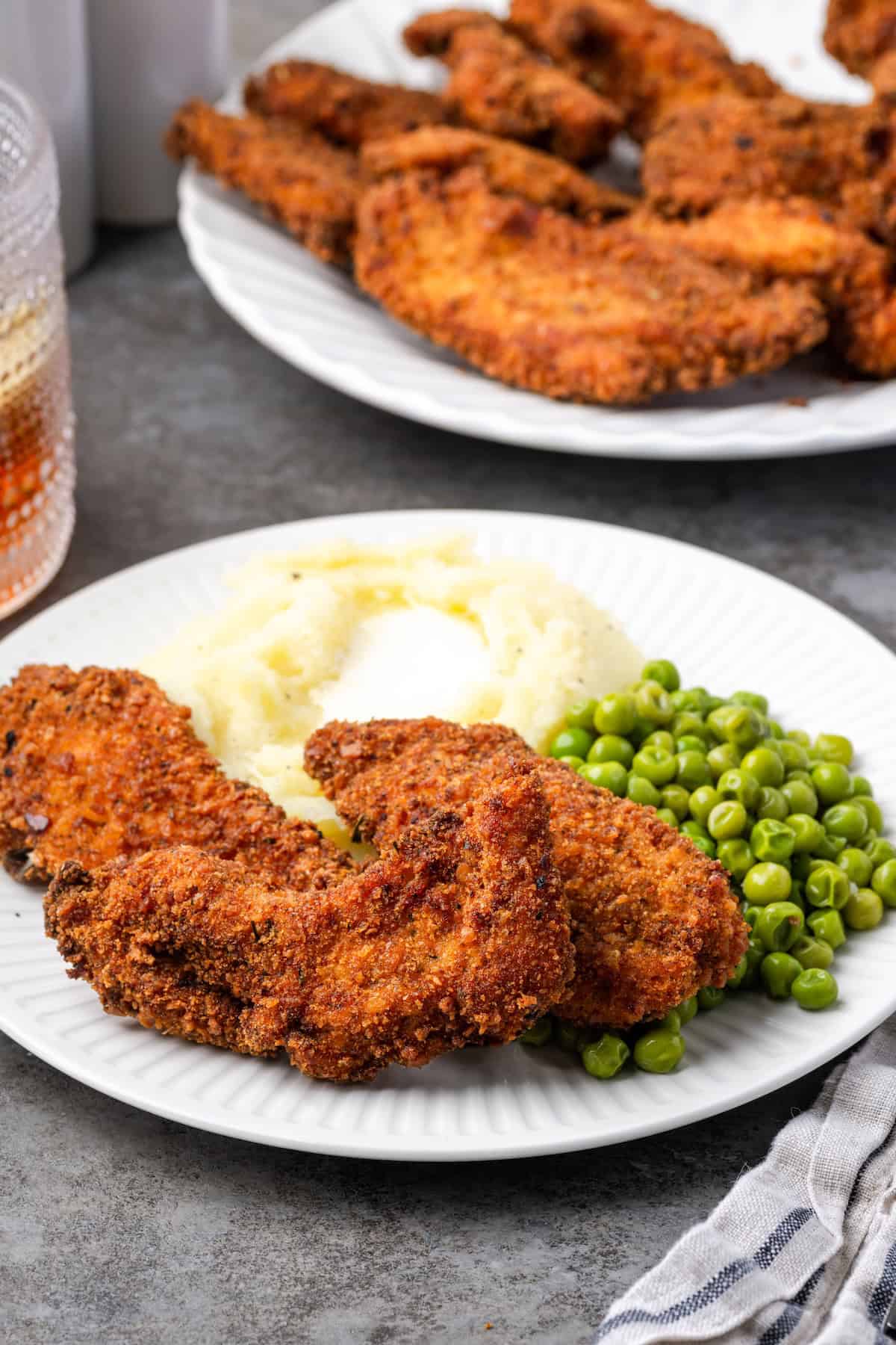 These extra crispy chicken tenders are breaded with chicken stuffing! It's an easy weeknight dinner hack, and you only need 3 ingredients! Crispy chicken tenders breaded with chicken stuffing next to mashed potatoes and peas on a plate, with a platter of chicken tenders in the background.